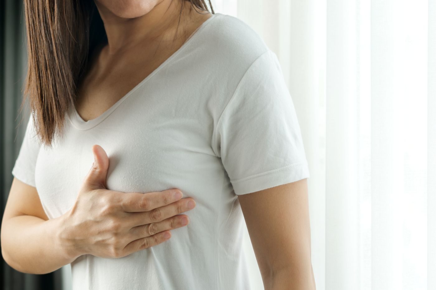 Mulher apalpando peito e pensando se um nódulo benigno pode se tornar maligno.