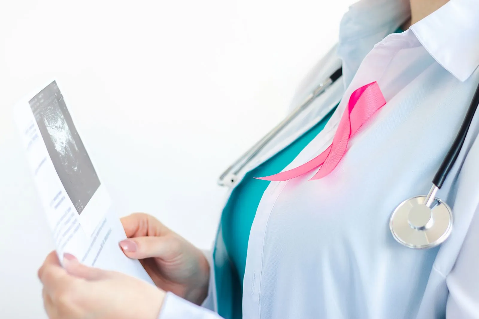 Médica com laço rosa analisa exames, representando o cuidado no diagnóstico da neoplasia de mama e a luta contra o câncer.
